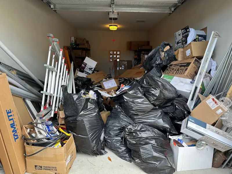 Garage packed with boxes, trash bags, ladders and old light fixtures, ready for a cleanout